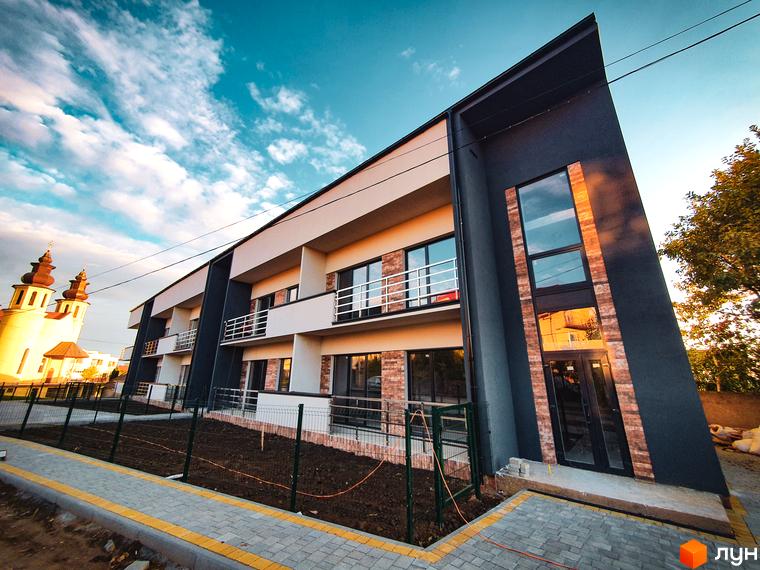 Зовнішній вигляд новобудови ЖК Клубний з сучасним дизайном фасаду та прибудинковою територією з огорожею та бруківкою.