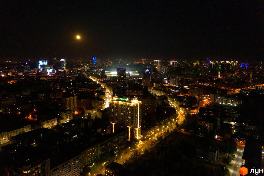 Житловий комплекс Тридцять восьма перлина вночі з освітленими фасадами. Вид на прибудинкову територію та місто з вулицями, наповненими світлом.