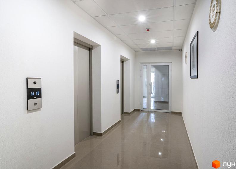 Сучасний коридор житлового комплексу Тридцять восьма перлина з ліфтами та великими вікнами. Світлі стіни та блискуча підлога створюють комфортну атмосферу.