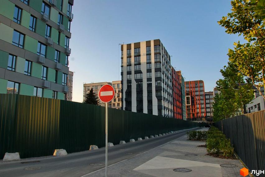 Житловий комплекс Respublika з багатоповерховими будинками зеленого, чорно-білого та червоно-оранжевого кольорів. Перед ними дорога, зелений паркан та доріжка з деревами.