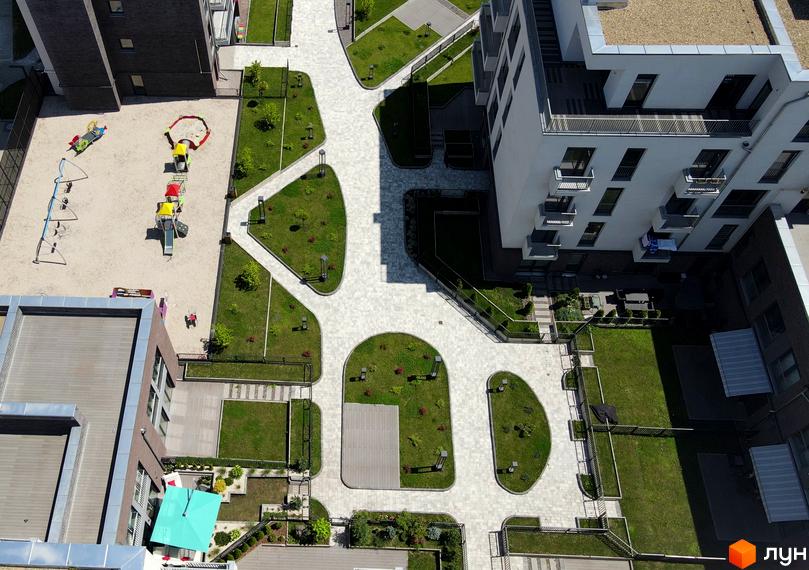 Житловий комплекс Villa Magnolia. Зовнішній вигляд білої будівлі з балконами та прибудинкова територія з дитячим майданчиком та зеленими зонами.