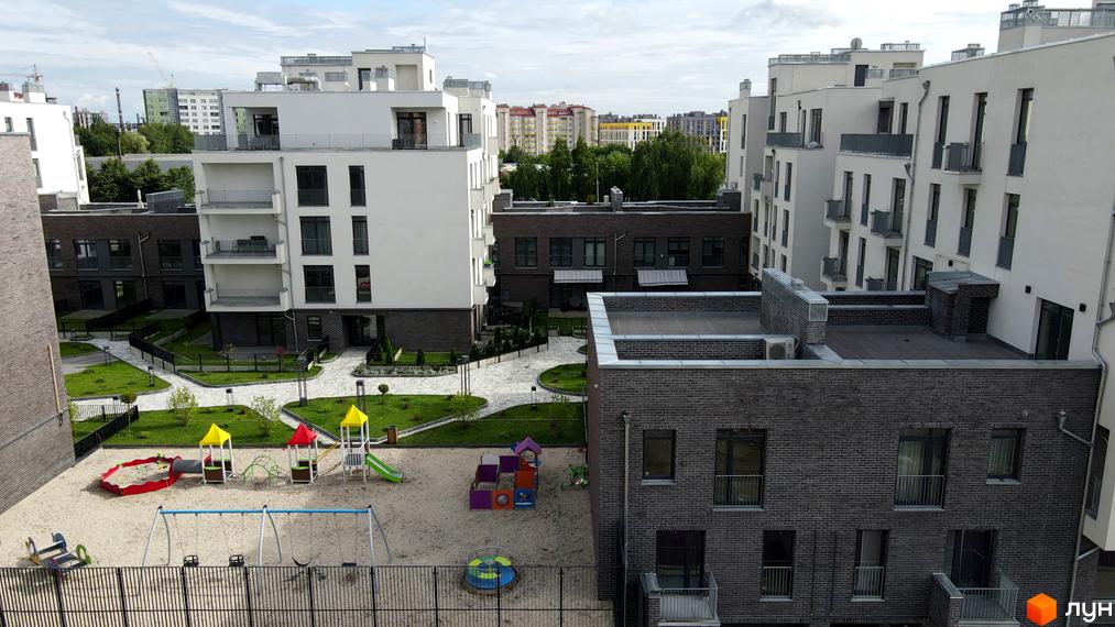 Житловий комплекс Villa Magnolia: білі та сірі будівлі з балконами, дитячий майданчик з пісочницею та гойдалками на піщаній території.