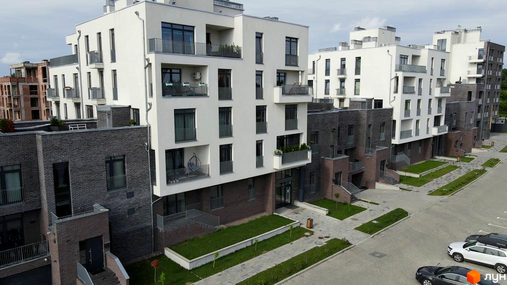 Новобудова ЖК Villa Magnolia з білими фасадами та темними цегляними елементами, балконами та прибудинковою територією з зеленими насадженнями та парковкою.