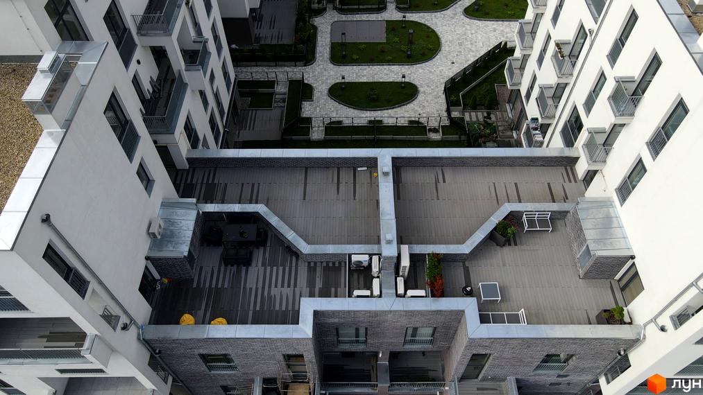 Житловий комплекс Villa Magnolia. Вид зверху на білосніжну будівлю з балконами та сірою терасою з меблями. Прибудинкова територія з доріжками та зеленими зонами.