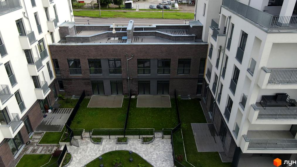 Зовнішній вигляд новобудови ЖК Villa Magnolia з цегляним фасадом та білими стінами. Прибудинкова територія з газоном та доріжками.