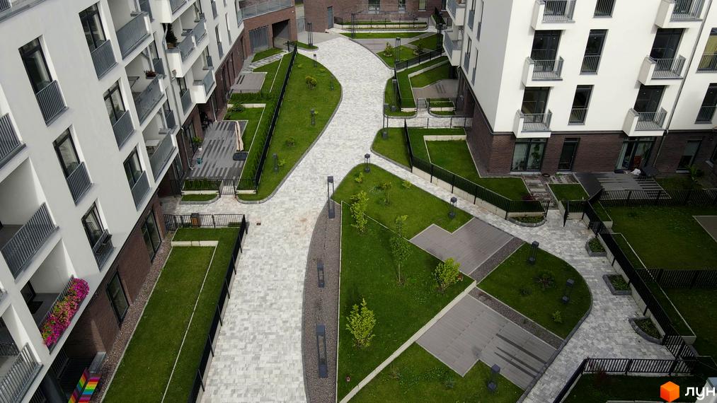 Зовнішній вигляд житлового комплексу Villa Magnolia з білими фасадами та сірими балконами. Прибудинкова територія з доглянутими газонами та пішохідними доріжками.