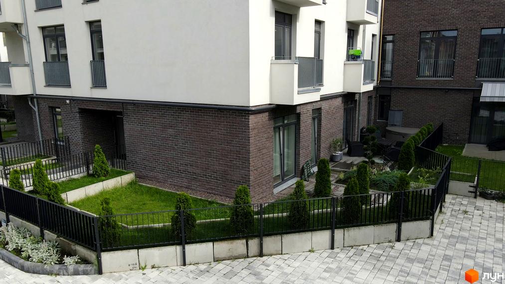 Зовнішній вигляд новобудови ЖК Villa Magnolia з цегляним фасадом та зеленими насадженнями навколо. Прибудинкова територія з доглянутим газоном та огорожею.