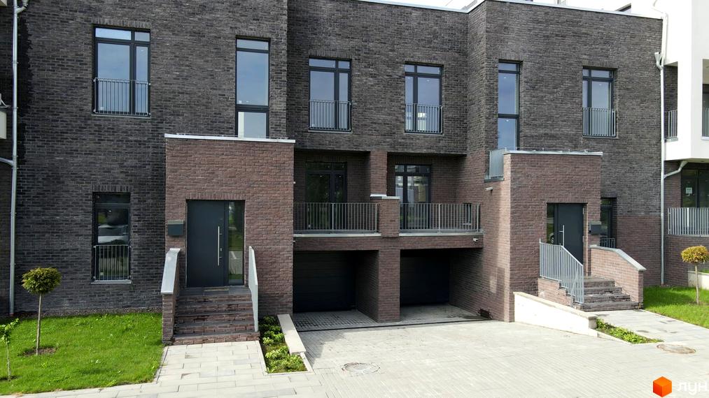 Фасад будинку житлового комплексу Villa Magnolia, оздоблений темною та цегляною плиткою, з балконами та гаражними воротами. Прибудинкова територія з газоном та бруківкою.