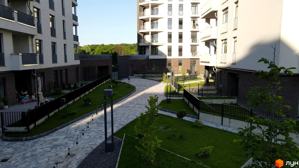 Зовнішній вигляд новобудови ЖК Villa Magnolia з бруківкою та зеленими насадженнями. Територія комплексу з доріжками для прогулянок та освітленням.