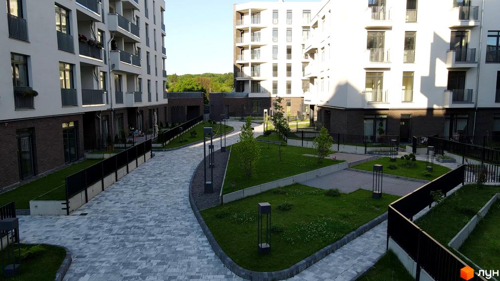 Житловий комплекс Villa Magnolia: фасади білих будинків з балконами та цегляною обробкою. Прибудинкова територія з бруківкою, газоном та ліхтарями.