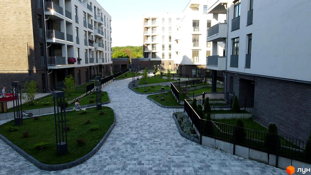 Житловий комплекс Villa Magnolia з білими фасадами та сірими балконами. Прибудинкова територія з бруківкою, газоном та дитячим майданчиком.