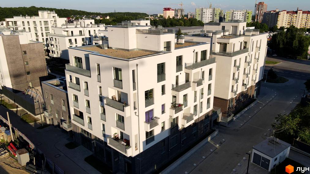 Зовнішній вигляд новобудови ЖК Villa Magnolia з білими фасадами та балконами. Прибудинкова територія з дорогою та зеленими насадженнями.