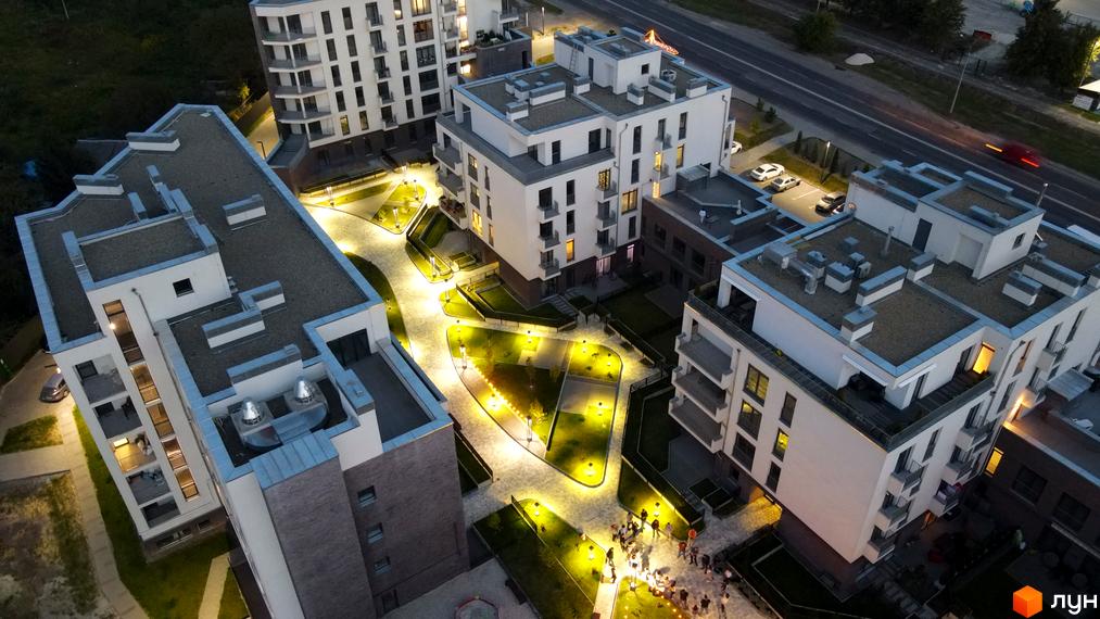 Житловий комплекс Villa Magnolia з білими фасадами та балконами, освітленою прибудинковою територією з доріжками та зеленими зонами. Новобудова з сучасним дизайном.