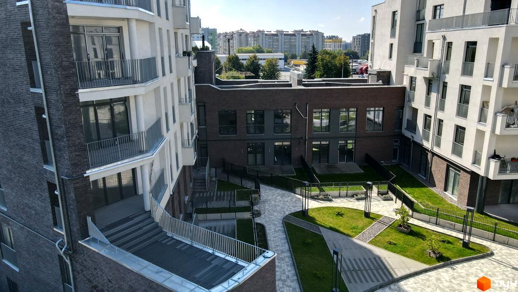 Житловий комплекс Villa Magnolia з білими та цегляними фасадами, балконами та прибудинковою територією з газоном та доріжками.