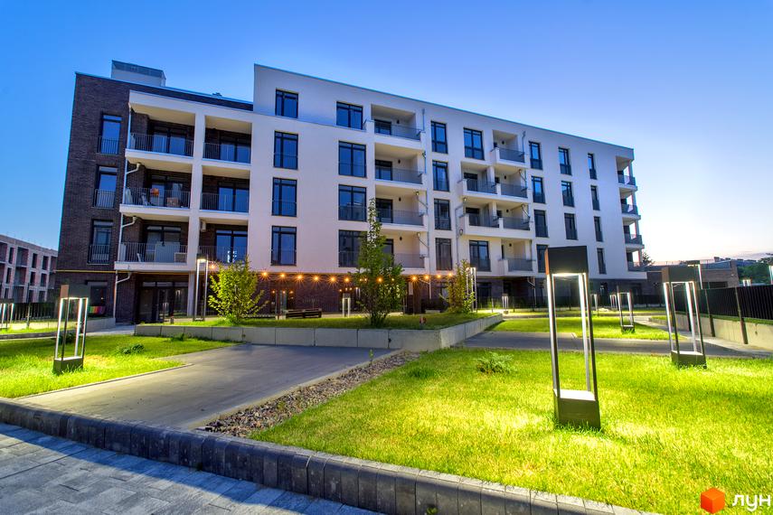 Зовнішній вигляд новобудови ЖК Villa Magnolia з цегляним фасадом та білою частиною. Прибудинкова територія з газоном та ліхтарями.