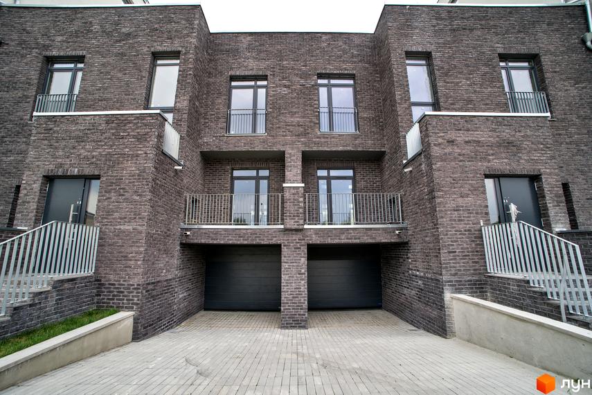 Новобудова ЖК Villa Magnolia з темної цегли з балконами та гаражними воротами. Перед будинком вимощена бруківкою доріжка та сходи з металевими перилами.