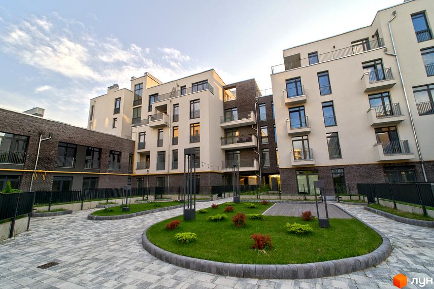 Зовнішній вигляд новобудови ЖК Villa Magnolia з цегляним та світлим фасадом, балконами та вікнами. Прибудинкова територія з доглянутим газоном, бруківкою та освітленням.