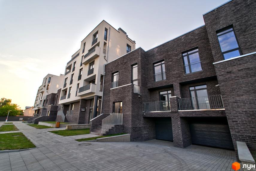 Новобудова ЖК Villa Magnolia з цегляним фасадом та білими вставками. Поруч доглянута прибудинкова територія з бруківкою та газоном.