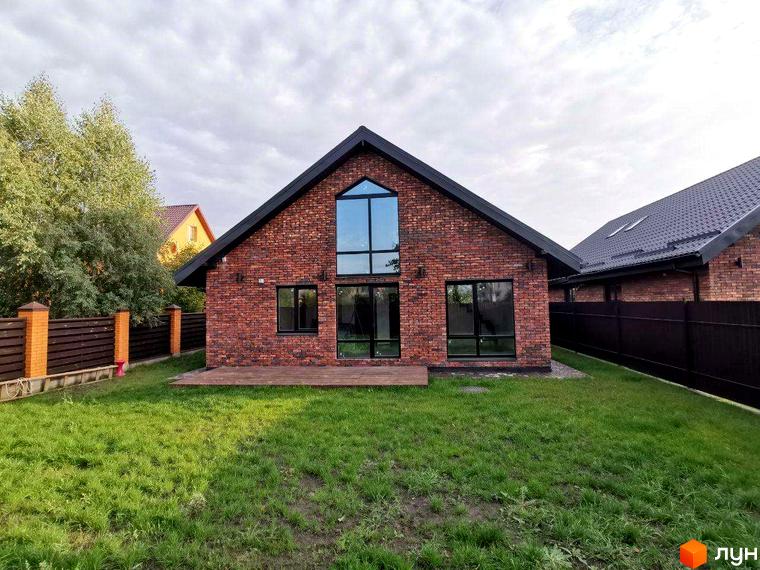 Котеджне містечко КМ Баварське село: цегляний будинок з великими вікнами та терасою на тлі зеленого газону та дерев.