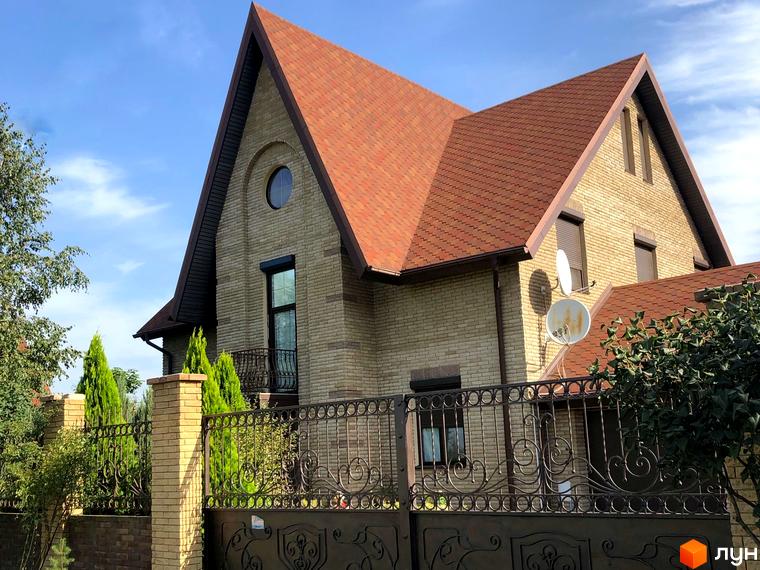 Котеджне містечко КМ Барвіта: двоповерховий будинок з червоним дахом та цегляними стінами, огороджений кованим парканом.