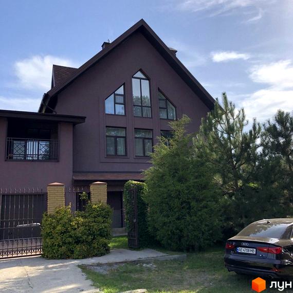 Котеджне містечко КМ Барвіта: коричневий будинок з великими трикутними вікнами та прибудинковою територією з деревами та автомобілем.