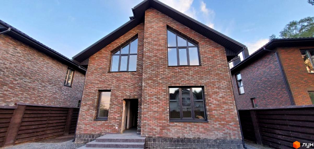 Котеджне містечко English village: двоповерховий цегляний будинок з великими трикутними вікнами та дерев'яним парканом.