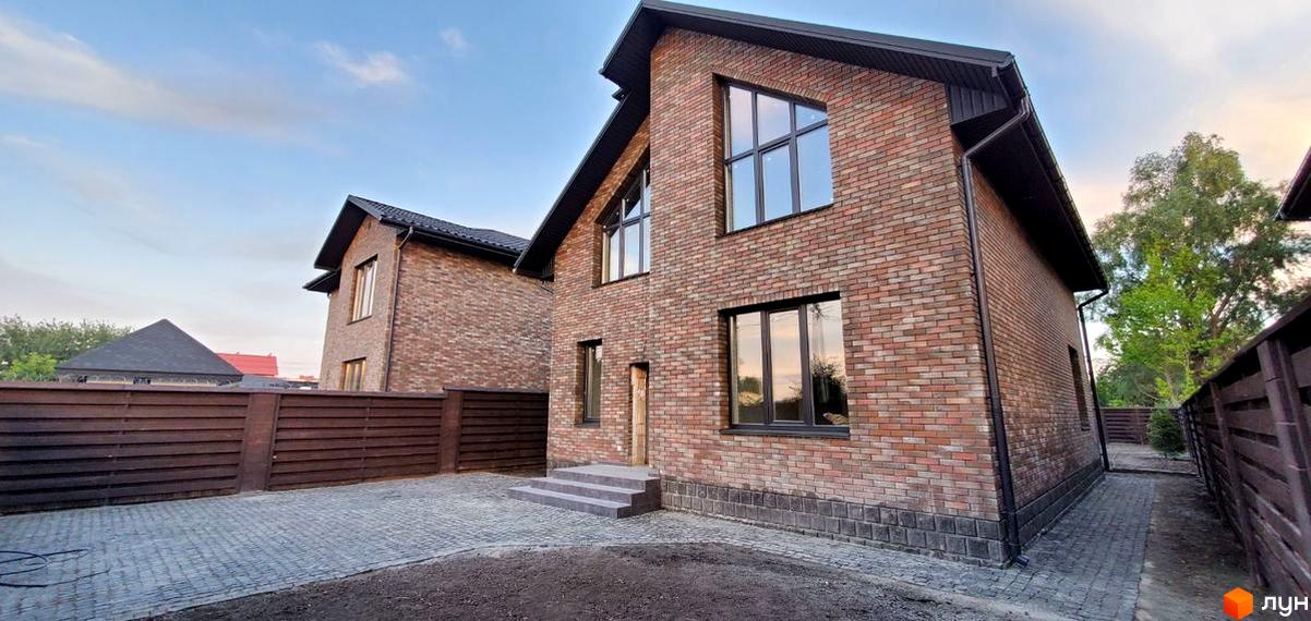 Котеджне містечко КМ English village: двоповерховий будинок з цегляним фасадом та великими вікнами, вимощена бруківкою прибудинкова територія та дерев'яний паркан.