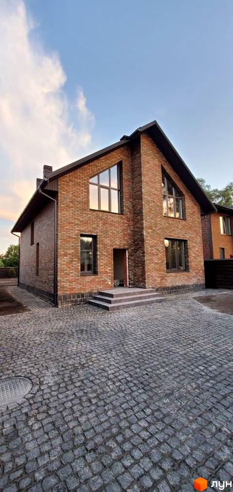 Зовнішній вигляд двоповерхового будинку з цегляним фасадом та великими вікнами. Прибудинкова територія вимощена бруківкою.