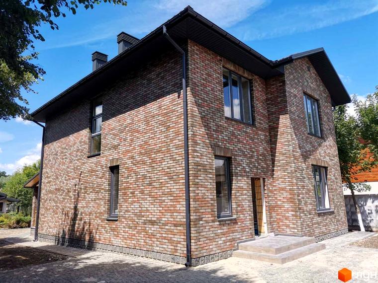Котеджне містечко КМ English village: двоповерховий будинок з цегляним фасадом та сірими вікнами. Територія навколо будинку вимощена плиткою, видно зелені насадження.