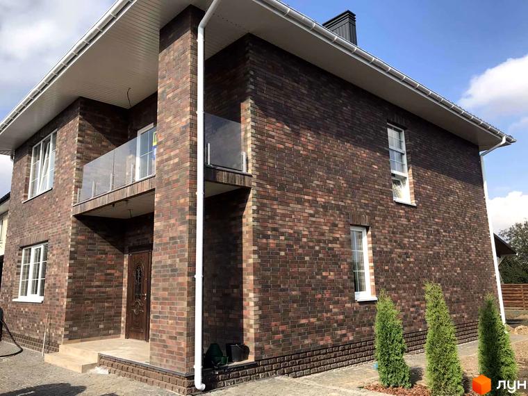 Котеджне містечко English village: двоповерховий будинок з цегляним фасадом, балконом зі скляним огородженням та акуратними зеленими насадженнями навколо.