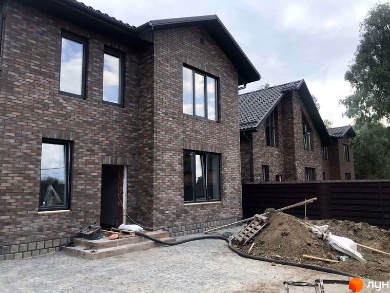 Зовнішній вигляд будинків з цегляним фасадом у котеджному містечку KМ English village. На прибудинковій території видно будівельні матеріали та елементи благоустрою.