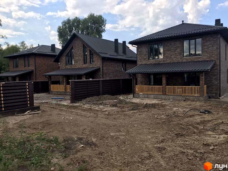 Котеджне містечко КМ English village: цегляні двоповерхові будинки з темним дахом та дерев'яними верандами, навколо будівельний майданчик з парканом.