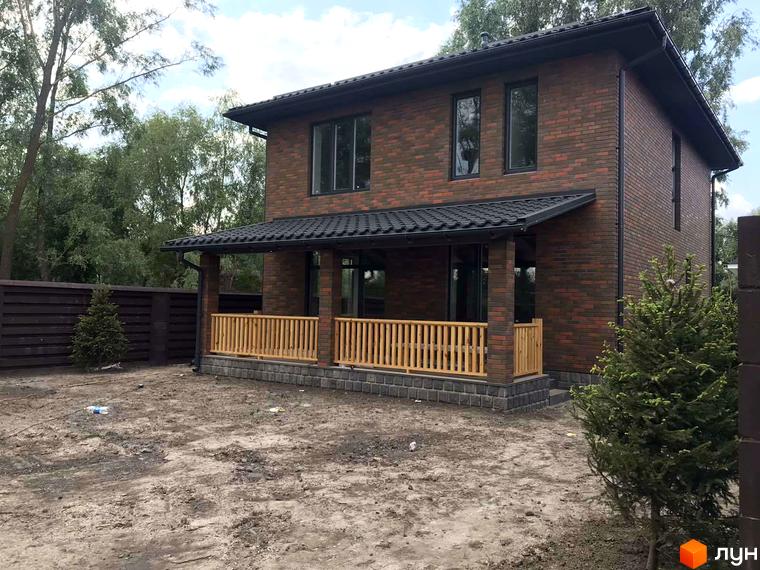 Котеджне містечко КМ English village: двоповерховий будинок з червоної цегли з навісом та дерев'яною огорожею на прибудинковій території з деревами та парканом.