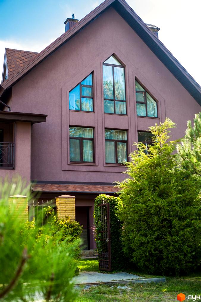 Котеджне містечко КМ Барвіта: фасад будинку з великими вікнами та зелена прибудинкова територія з деревами та воротами.