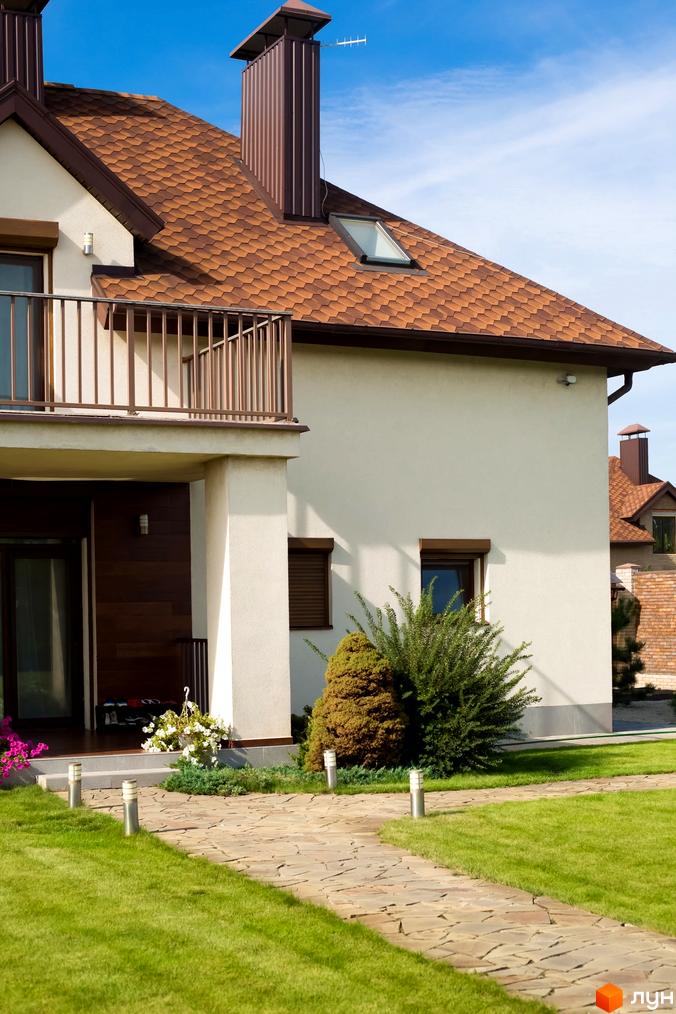 Котеджне містечко КМ Барвіта: двоповерховий будинок з коричневим дахом та балконом, доглянута прибудинкова територія з доріжкою та газоном.