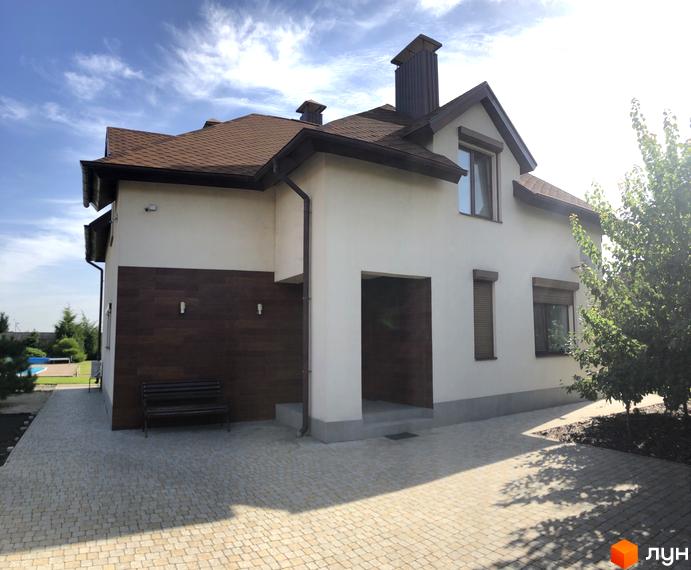 Котеджне містечко Барвіта: двоповерховий будинок з коричневим дахом та дерев'яним оздобленням фасаду, вимощена бруківкою прибудинкова територія та зелені насадження.