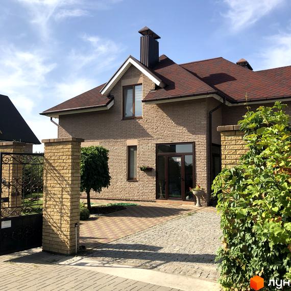 Котеджне містечко КМ Барвіта: двоповерховий будинок з коричневою черепичною покрівлею та цегляним фасадом, огороджена територія з кованою брамою та бруківкою.