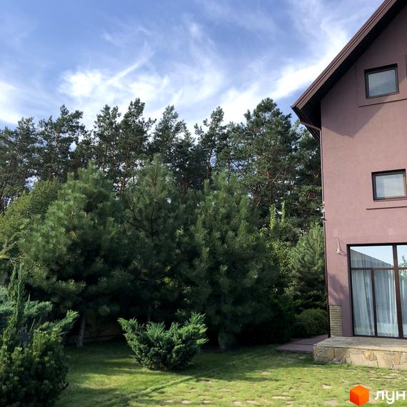 Котеджне містечко КМ Барвіта: двоповерховий будинок з коричневим фасадом та вікнами, оточений зеленню та соснами.