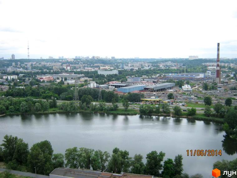 Панорамний вид на житловий комплекс Гранд з висоти пташиного польоту, що демонструє його розташування біля водойми та промислової зони. Навколо комплексу багато зелені та дерев.