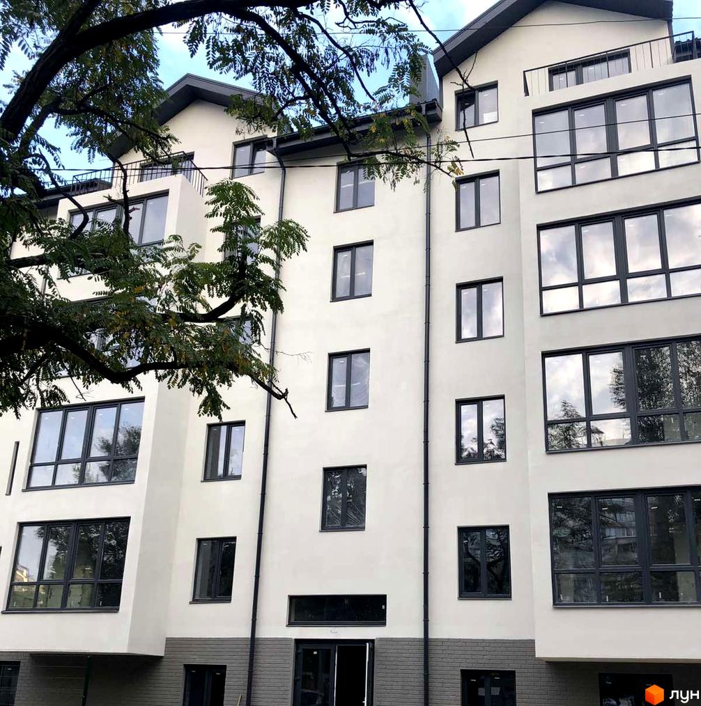 Фасад клубного будинку «Зразковий» з великими вікнами та балконами. Будинок оточений деревами.