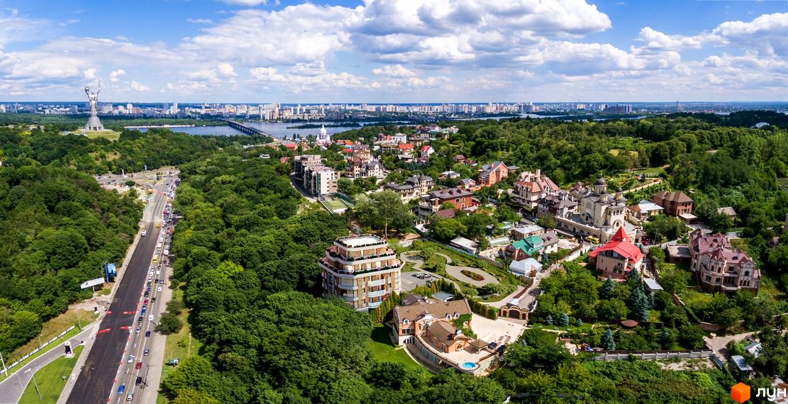 Вид на житловий комплекс з висоти пташиного польоту, що демонструє його унікальну архітектуру та зелену прибудинкову територію з доглянутими ландшафтами.