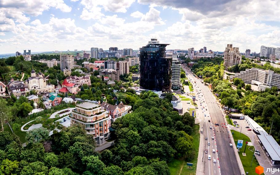 Вид на житловий комплекс на вул. Ломаківська (Мічуріна), 19б з сучасною архітектурою та зеленою прибудинковою територією. Навколо комплексу розташовані дерева та міський пейзаж.