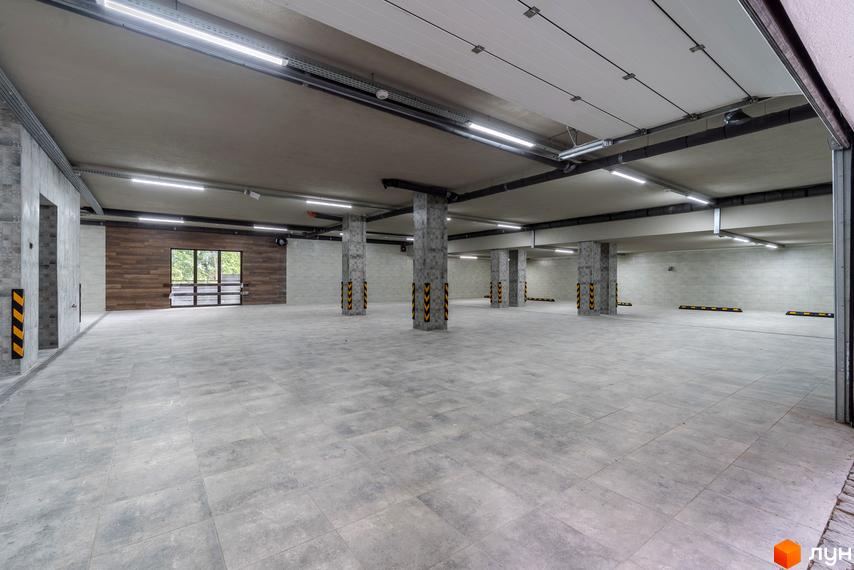 Підземний паркінг житлового комплексу на вул. Ломаківська (Мічуріна), 19б. Просторе приміщення з бетонними колонами, плитковою підлогою та яскравим освітленням.