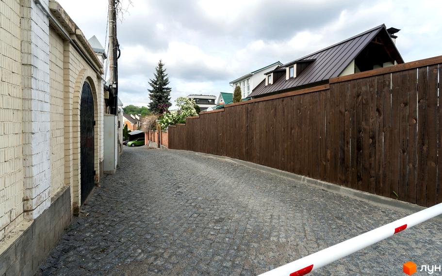 Вулиця Ломаківська (Мічуріна), 19б: кам'яний паркан та бруківка вздовж житлового комплексу. Зелений автомобіль біля будинку.