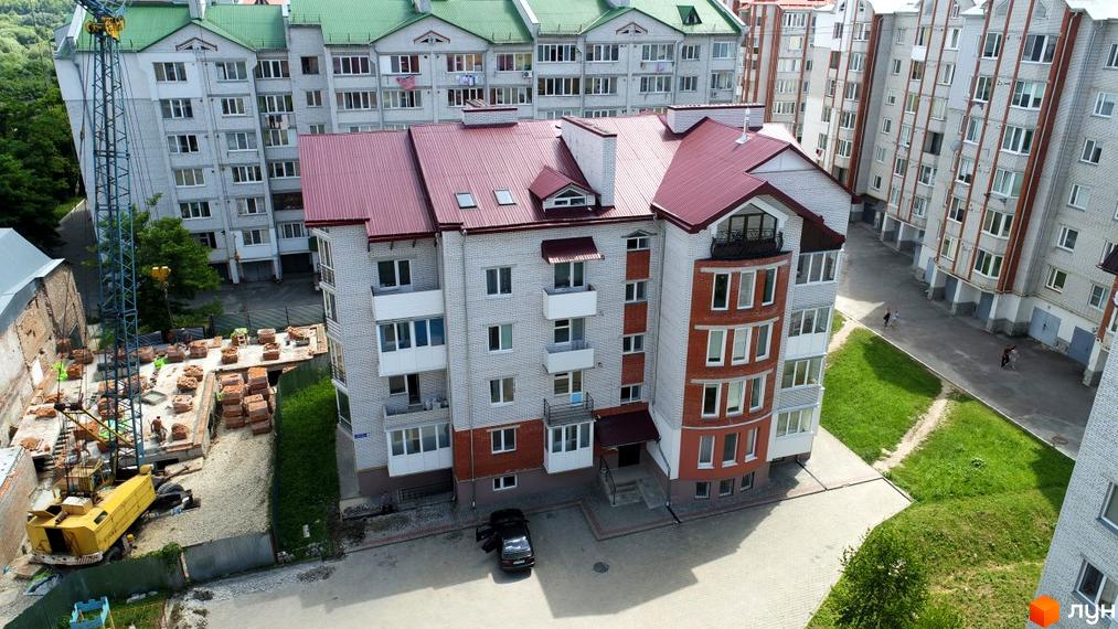 Зовнішній вигляд житлового комплексу на пров. Цегельний, 3, з цегляним фасадом та червоним дахом, поруч будівельний майданчик з краном та будматеріалами.