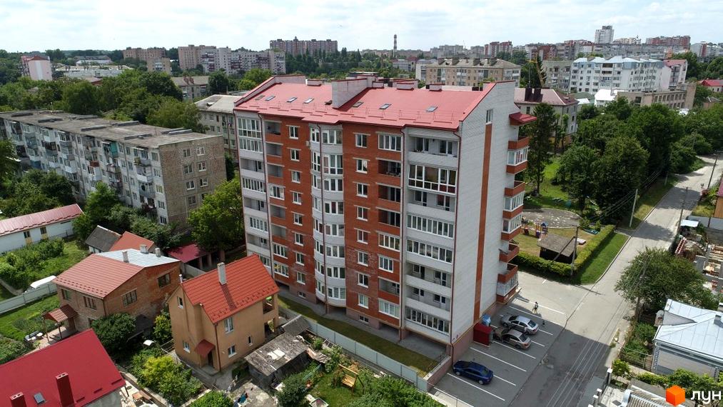 Зовнішній вигляд багатоповерхового будинку з червоним дахом та цегляним фасадом на вулиці Виговського, 3а. Прибудинкова територія з парковкою та зеленими зонами.