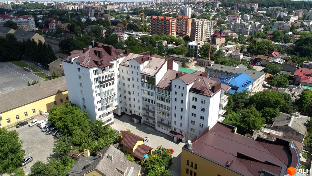 Вид на багатоповерхові будинки житлового комплексу по вулиці Бродівська, 13, з білими фасадами та коричневими дахами, на тлі міського пейзажу та зелені.
