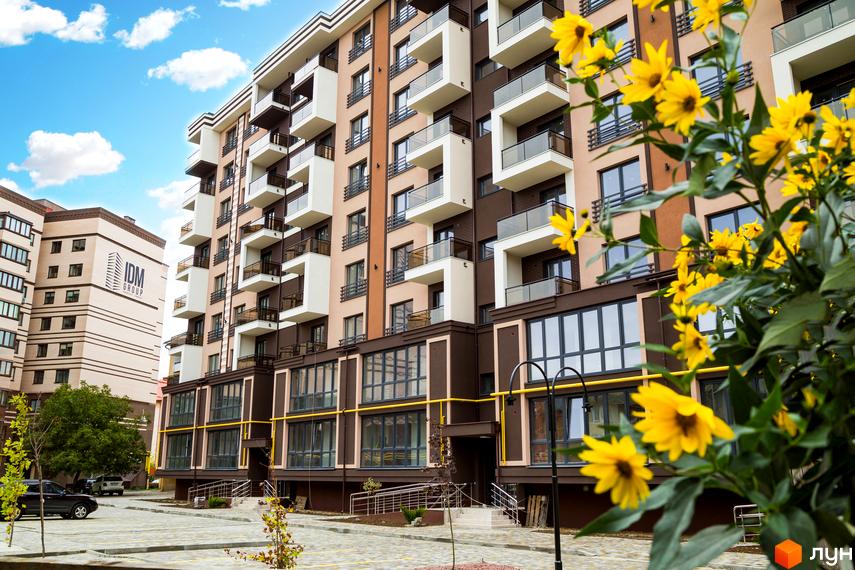 Зовнішній вигляд житлового комплексу Modern. Багатоповерховий будинок з балконами та великими вікнами, прибудинкова територія з квітами.