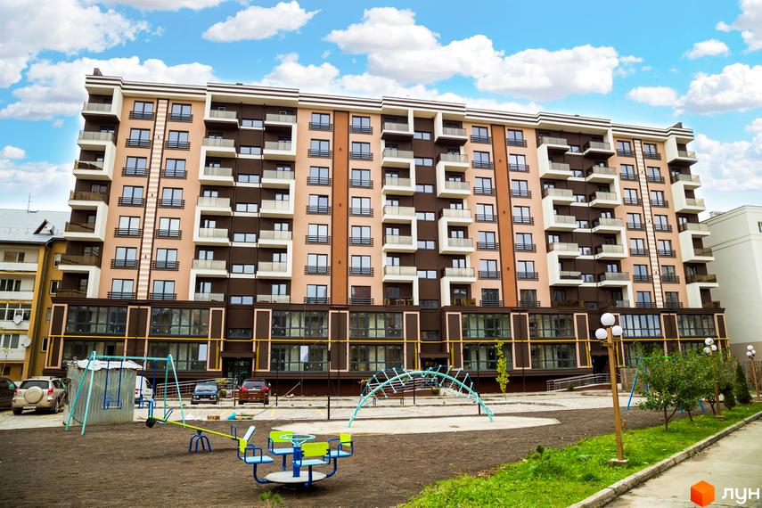 Зображення фасаду та прибудинкової території Житлового комплексу Modern. Багатоповерхова будівля з дитячим майданчиком на передньому плані.
