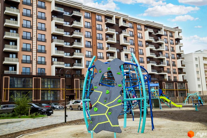 Зображення фасаду Житлового комплексу Modern та дитячого майданчика. Багатоповерховий будинок з балконами та ігровий комплекс для дітей.